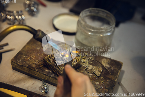 Image of Close up hands of jeweller, goldsmiths making of silver ring with gemstone using professional tools.