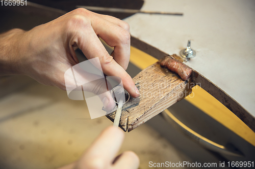 Image of Close up hands of jeweller, goldsmiths making of silver ring with gemstone using professional tools.