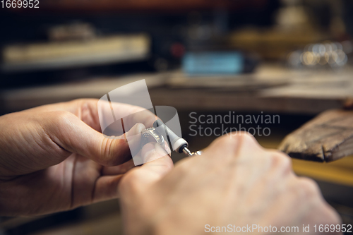 Image of Close up hands of jeweller, goldsmiths making of silver ring with gemstone using professional tools.