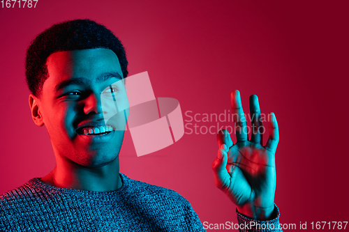 Image of African-american man\'s portrait isolated on red studio background in multicolored neon light