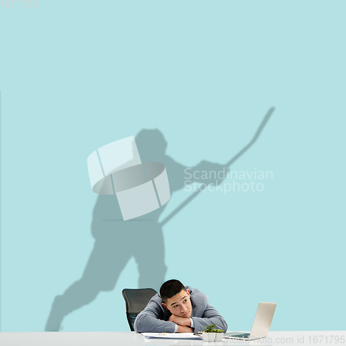Image of Young man dreaming about future in big sport during his work in office. Becoming a legend. Shadow of dreams on the wall behind him. Copyspace.