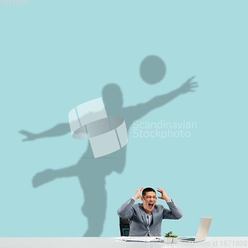 Image of Young man dreaming about future in big sport during his work in office. Becoming a legend. Shadow of dreams on the wall behind him. Copyspace.
