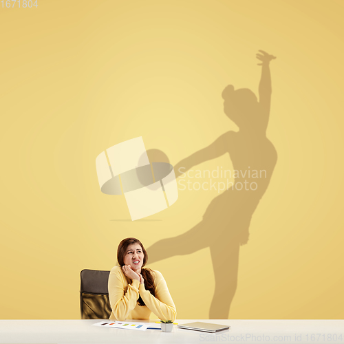 Image of Young woman dreaming about future in big sport during her work in office. Becoming a legend. Shadow of dreams on the wall behind her. Copyspace.