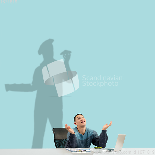 Image of Young man dreaming about future in big culinary during his work in office. Becoming a legend. Shadow of dreams on the wall behind him. Copyspace.