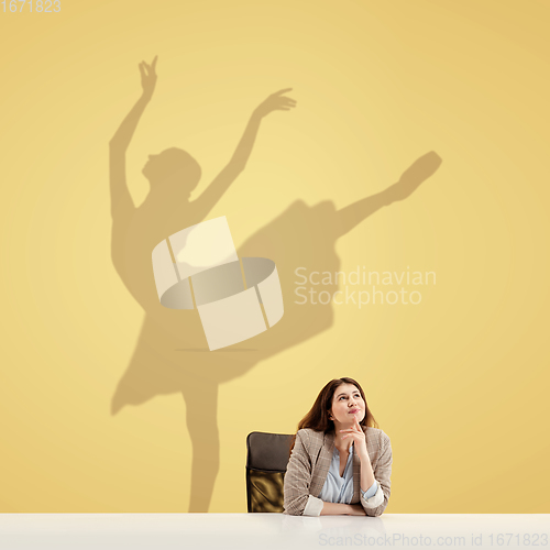 Image of Young woman dreaming about future in big sport during her work in office. Becoming a legend. Shadow of dreams on the wall behind her. Copyspace.