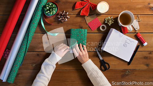 Image of hands wrapping christmas gift into paper at home