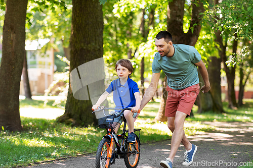 Image of father teaching little son to ride bicycle at park