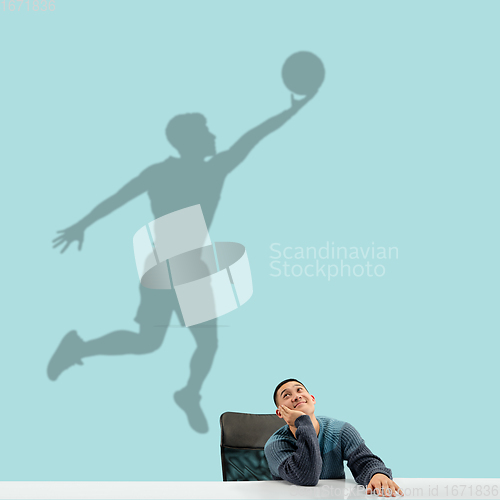 Image of Young man dreaming about future in big sport during his work in office. Becoming a legend. Shadow of dreams on the wall behind him. Copyspace.