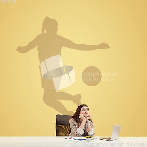 Image of Young woman dreaming about future in big sport during her work in office. Becoming a legend. Shadow of dreams on the wall behind her. Copyspace.