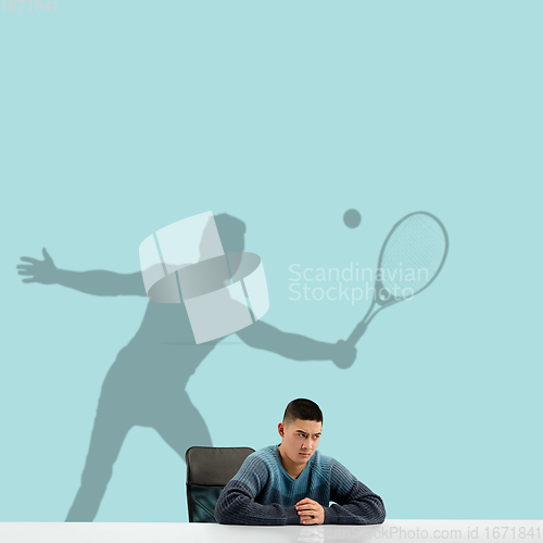 Image of Young man dreaming about future in big sport during his work in office. Becoming a legend. Shadow of dreams on the wall behind him. Copyspace.
