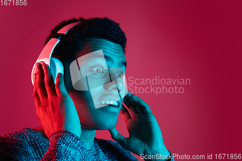 Image of African-american man\'s portrait isolated on red studio background in multicolored neon light