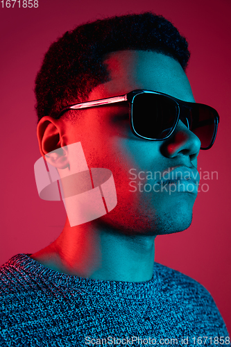 Image of African-american man\'s portrait isolated on red studio background in multicolored neon light