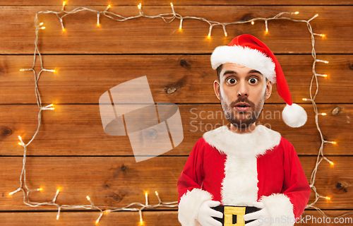 Image of surprised santa over garland on wooden background