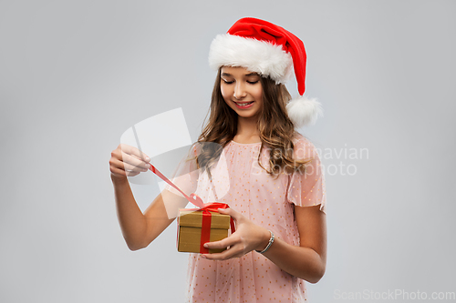 Image of teenage girl in santa hat opening christmas gift