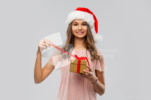 Image of teenage girl in santa hat opening christmas gift