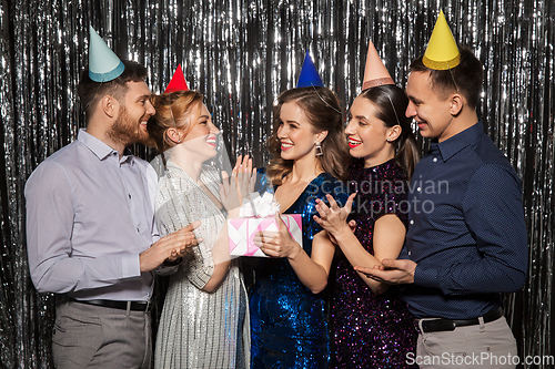 Image of happy friends in party hats with birthday gift