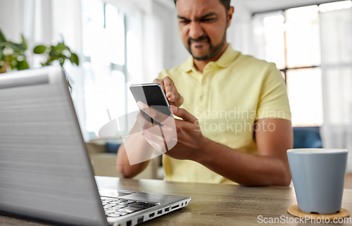 Image of angry indian man with smartphone working at home