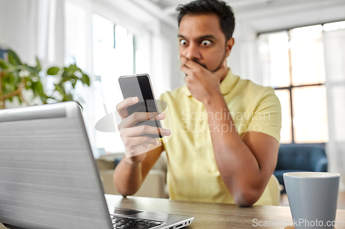 Image of shocked indian man with smartphone working at home