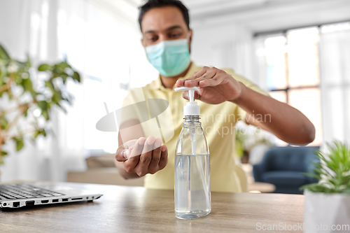 Image of man in mask using hand sanitizer at home office