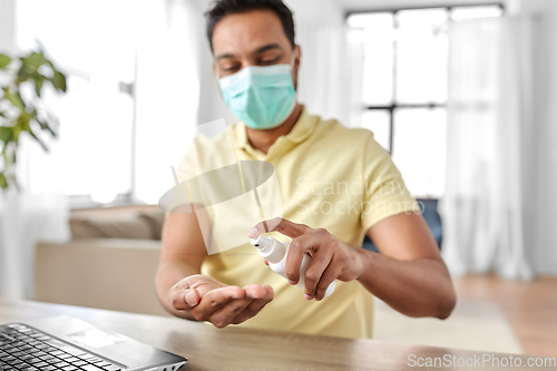 Image of man in mask using hand sanitizer at home office