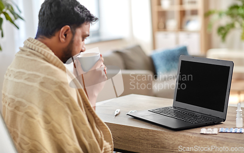 Image of sick indian man with laptop drinking tea at home