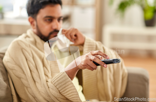 Image of sick man with paper tissue and tv remote at home