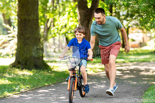 Image of father teaching little son to ride bicycle at park