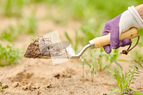 Image of hand digging flowerbed ground with garden trowel