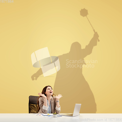 Image of Young woman dreaming about fantasy worlds during her work in office. Becoming a legend. Shadow of dreams on the wall behind her. Copyspace.