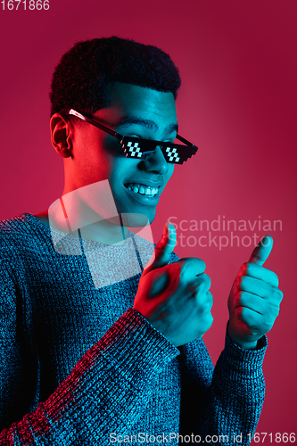 Image of African-american man\'s portrait isolated on red studio background in multicolored neon light