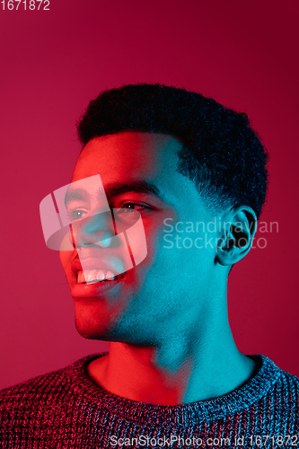 Image of African-american man\'s portrait isolated on red studio background in multicolored neon light