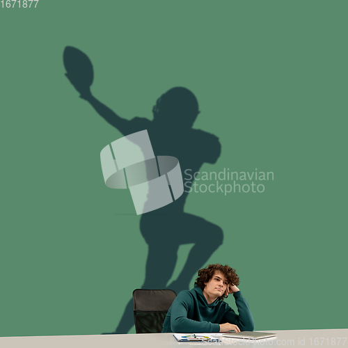 Image of Young man dreaming about future in big sport during his work in office. Becoming a legend. Shadow of dreams on the wall behind him. Copyspace.