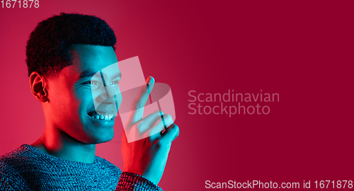 Image of African-american man\'s portrait isolated on red studio background in multicolored neon light