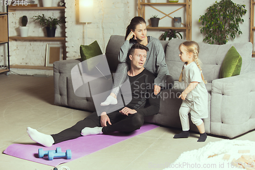 Image of Young family resting after exercising fitness, aerobic, yoga at home, sporty lifestyle. Getting active during lockdown, quarantine. Home gym.