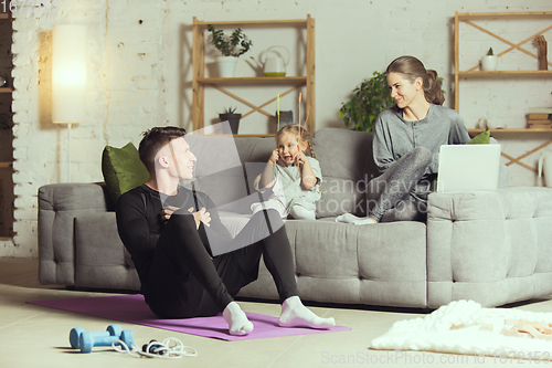 Image of Young family resting after exercising fitness, aerobic, yoga at home, sporty lifestyle. Getting active during lockdown, quarantine. Home gym.