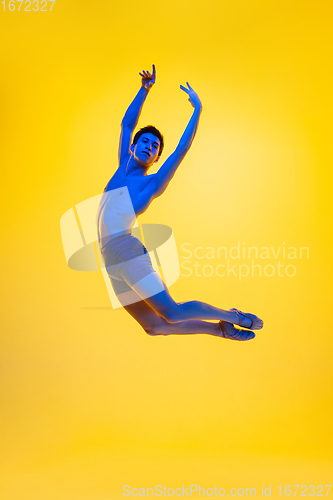 Image of Young and graceful ballet dancer isolated on yellow studio background in neon light. Art, motion, action, flexibility, inspiration concept.