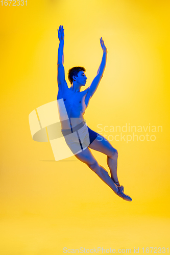 Image of Young and graceful ballet dancer isolated on yellow studio background in neon light. Art, motion, action, flexibility, inspiration concept.