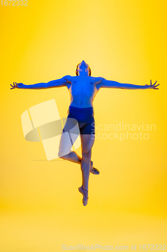 Image of Young and graceful ballet dancer isolated on yellow studio background in neon light. Art, motion, action, flexibility, inspiration concept.
