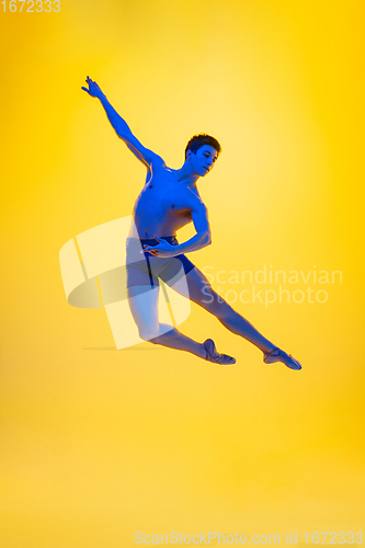 Image of Young and graceful ballet dancer isolated on yellow studio background in neon light. Art, motion, action, flexibility, inspiration concept.