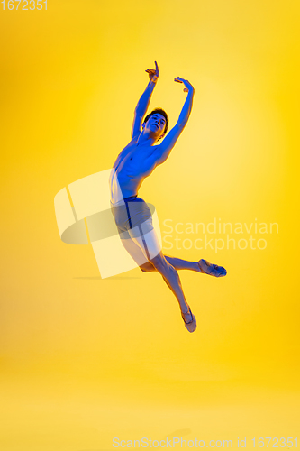 Image of Young and graceful ballet dancer isolated on yellow studio background in neon light. Art, motion, action, flexibility, inspiration concept.