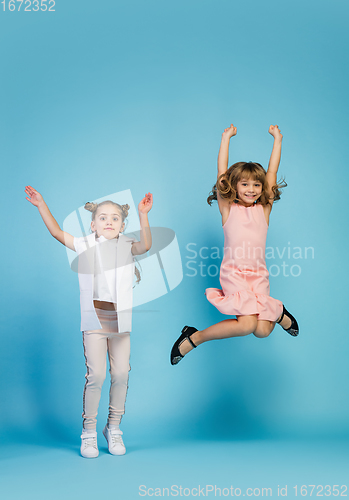 Image of Happy kids, girls isolated on blue studio background. Look happy, cheerful, sincere. Copyspace. Childhood, education, emotions concept