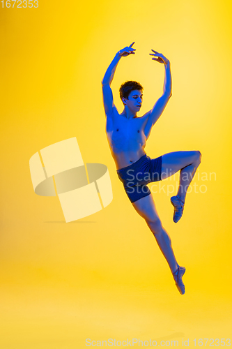 Image of Young and graceful ballet dancer isolated on yellow studio background in neon light. Art, motion, action, flexibility, inspiration concept.