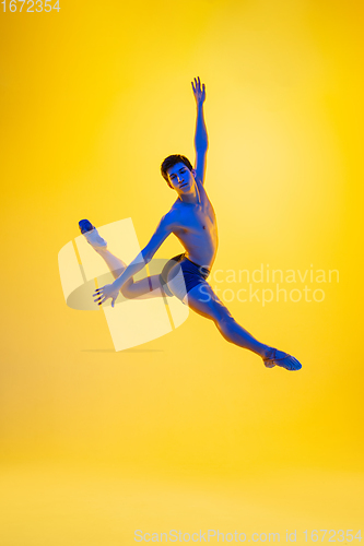 Image of Young and graceful ballet dancer isolated on yellow studio background in neon light. Art, motion, action, flexibility, inspiration concept.