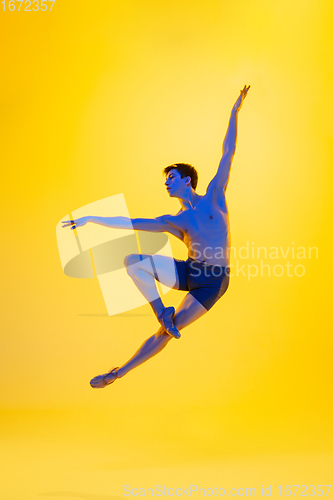 Image of Young and graceful ballet dancer isolated on yellow studio background in neon light. Art, motion, action, flexibility, inspiration concept.