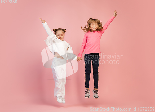 Image of Happy kids, girls isolated on coral pink studio background. Look happy, cheerful, sincere. Copyspace. Childhood, education, emotions concept