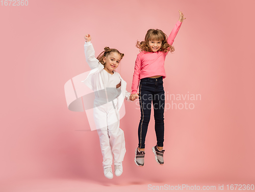 Image of Happy kids, girls isolated on coral pink studio background. Look happy, cheerful, sincere. Copyspace. Childhood, education, emotions concept