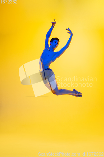 Image of Young and graceful ballet dancer isolated on yellow studio background in neon light. Art, motion, action, flexibility, inspiration concept.