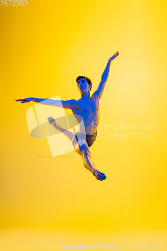 Image of Young and graceful ballet dancer isolated on yellow studio background in neon light. Art, motion, action, flexibility, inspiration concept.