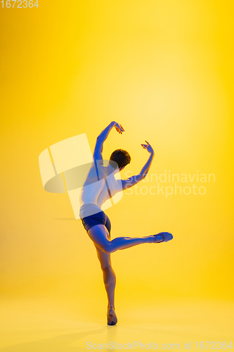 Image of Young and graceful ballet dancer isolated on yellow studio background in neon light. Art, motion, action, flexibility, inspiration concept.
