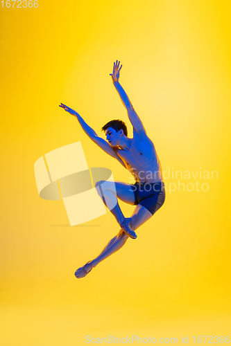 Image of Young and graceful ballet dancer isolated on yellow studio background in neon light. Art, motion, action, flexibility, inspiration concept.